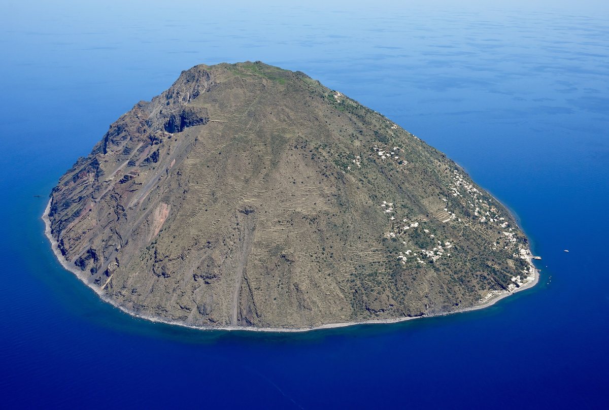 The volcanic island of Alicudi seen from the air, its terraced slopes rising out of a deep blue sea.