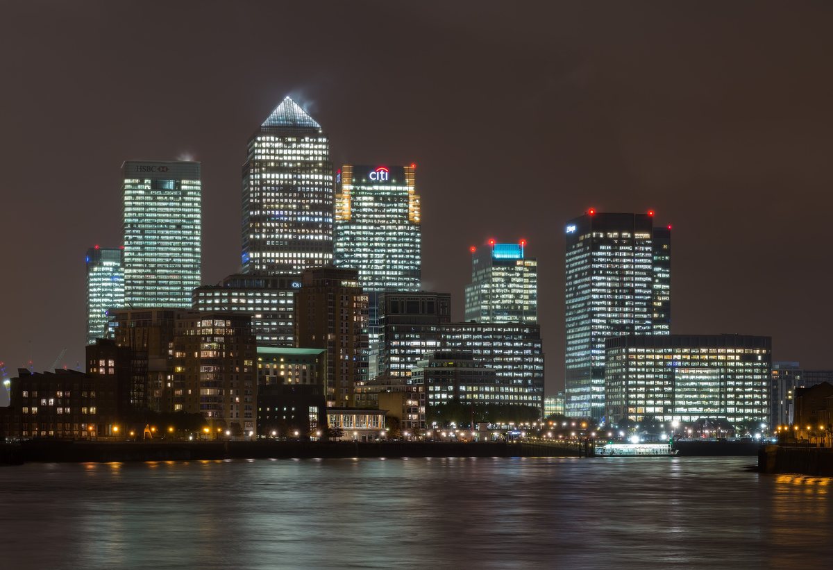 The towers of Canary Wharf lit at night above the dark water of the Thames.