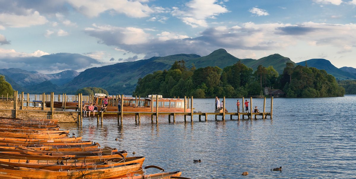 Rowing boats moored on Derwent Water with wooded fells beyond, in the Lake District.