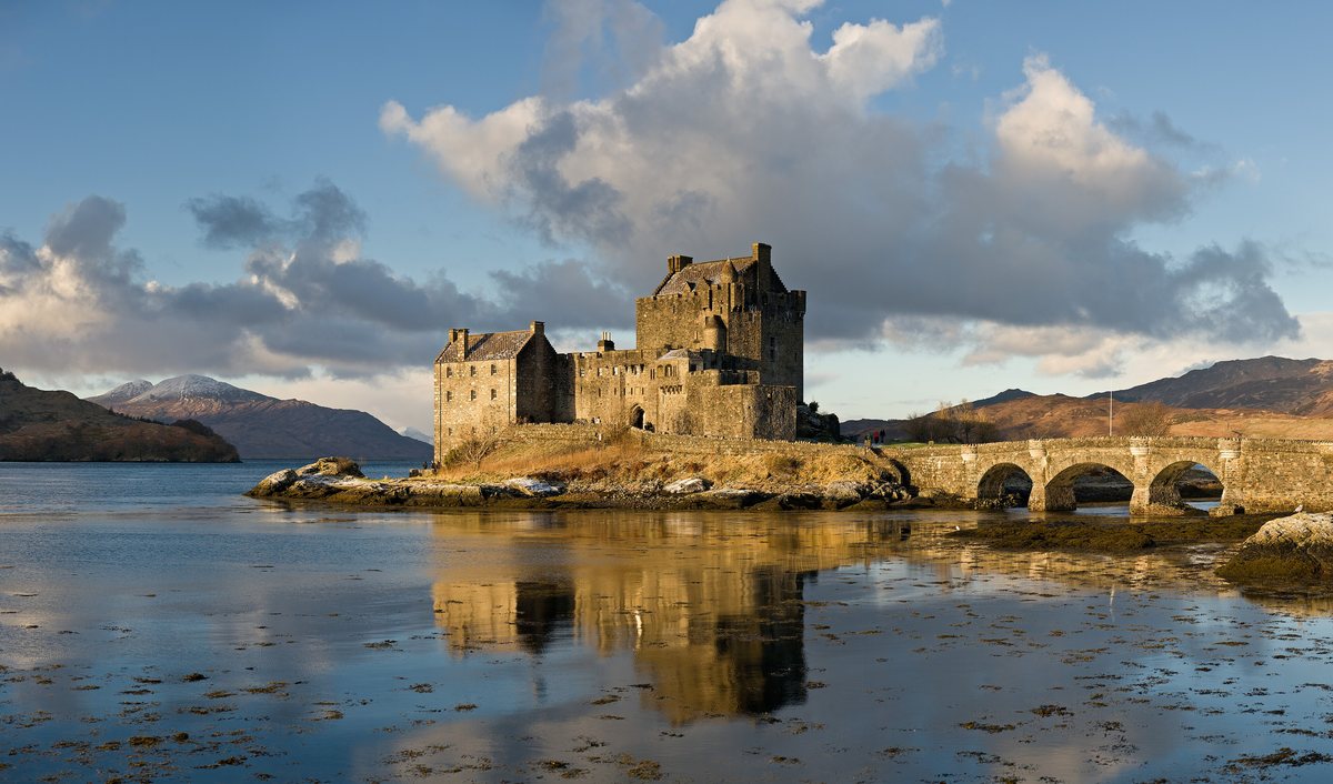 Eilean Donan Castle and its stone bridge reflected in still loch water under a bright winter sky.