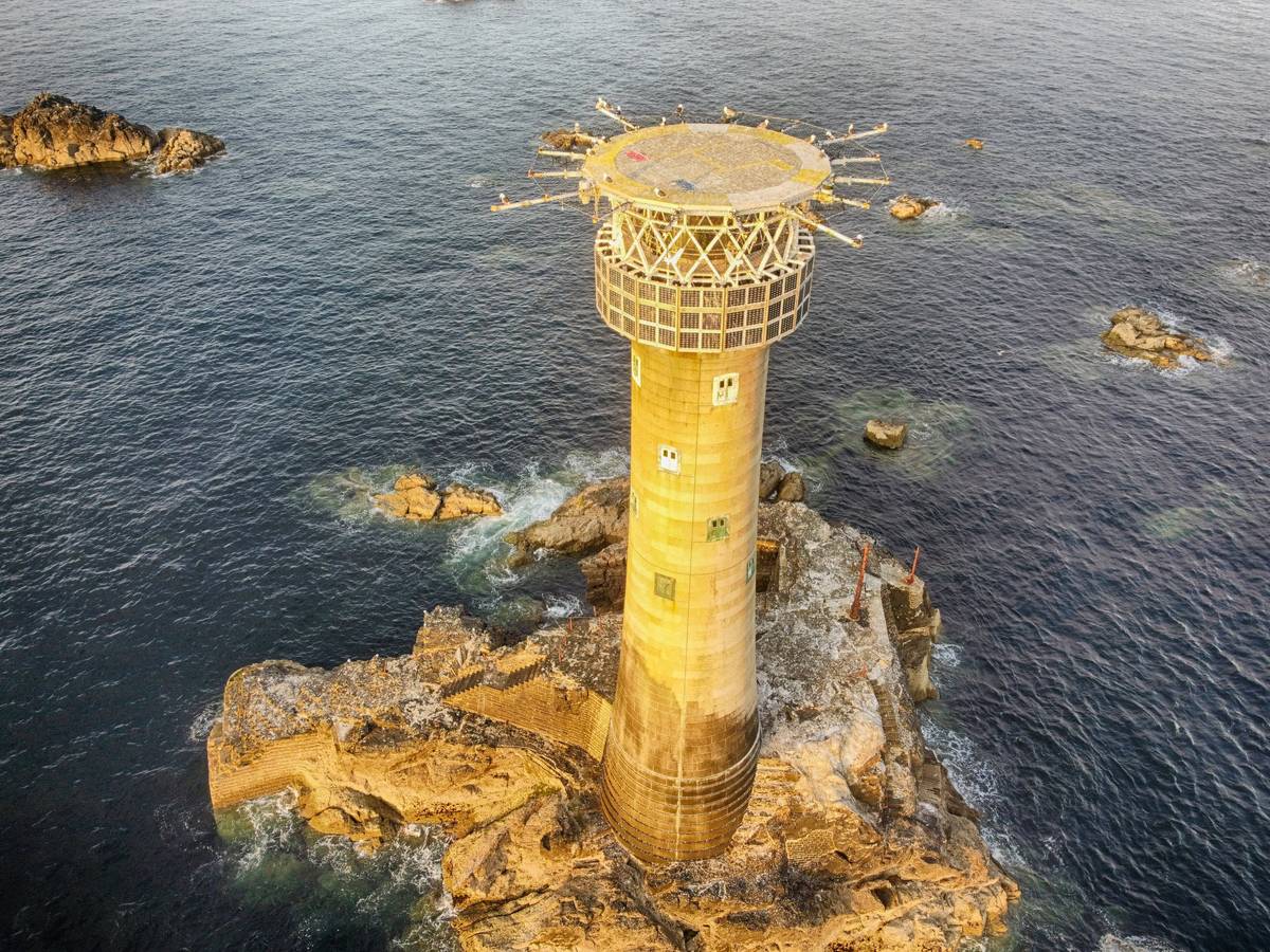 Longships Lighthouse on its granite reef, seen from the air above the surrounding dark sea.