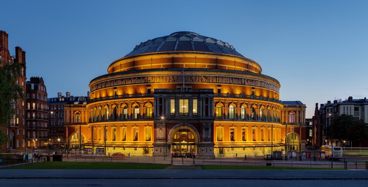 The domed Royal Albert Hall glowing with warm light at dusk.