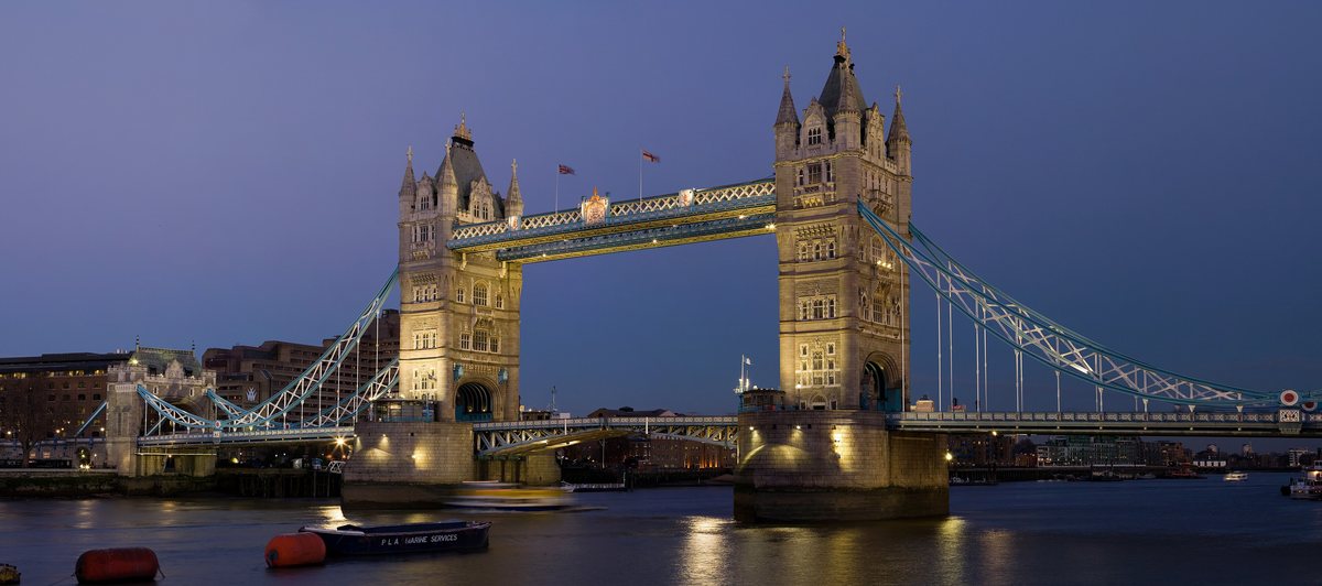 Tower Bridge lit up at dusk against a deep blue sky, reflected in the River Thames.