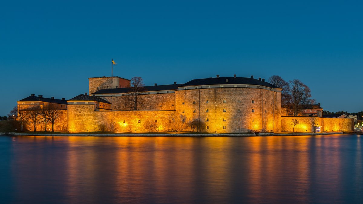 The granite walls of Vaxholm Fortress lit warm at blue hour, reflected in the calm water of the Stockholm archipelago.