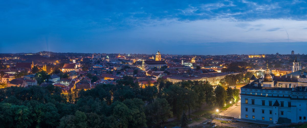 The rooftops and church towers of Vilnius Old Town under a blue evening sky.