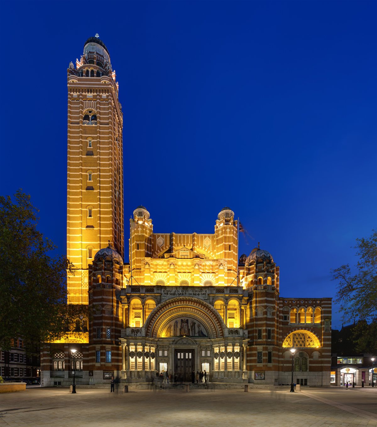 The striped brick facade and campanile of Westminster Cathedral, floodlit against a dusk sky.